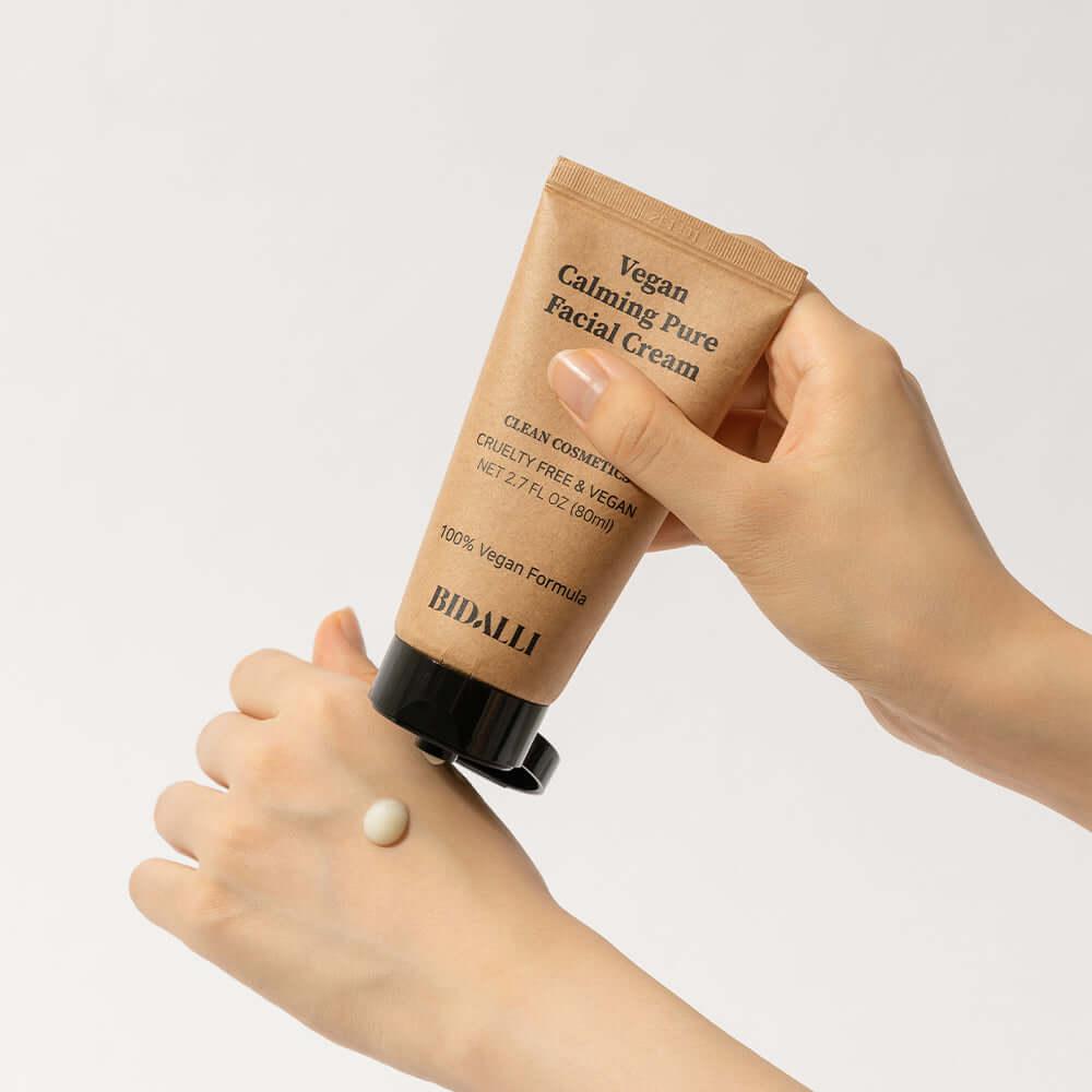 Person applying BIDALLI Vegan Calming Pure Facial Cream onto the back of their hand, showcasing a small dollop of cream and the product tube