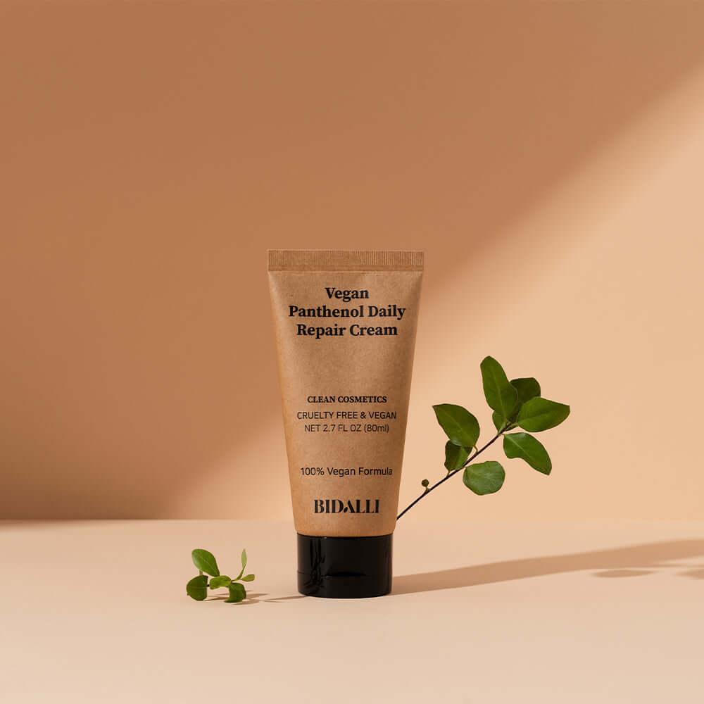 Bidalli Vegan Panthenol Daily Repair Cream standing against a warm beige background with green leaves, highlighting its natural and vegan formulation