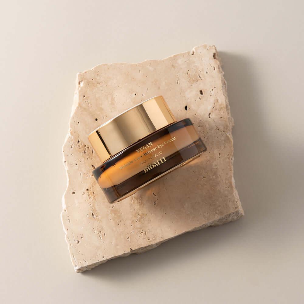 Bidalli Vegan Wrinkle-Care Intense Eye Cream in amber jar with gold lid, placed on natural stone slab, luxurious anti-aging eye treatment with vegan formula