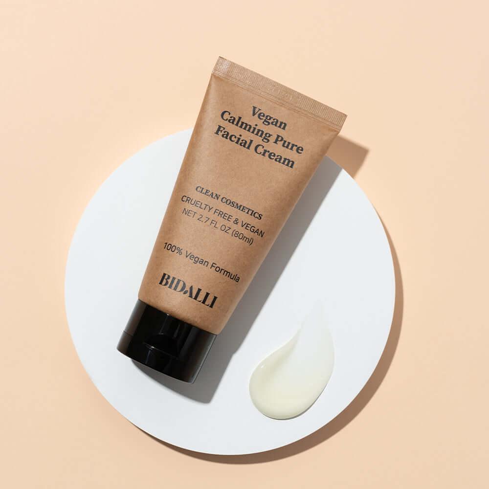 BIDALLI Vegan Calming Pure Facial Cream tube displayed with a dollop of creamy white texture on a white circle platform over a peach background