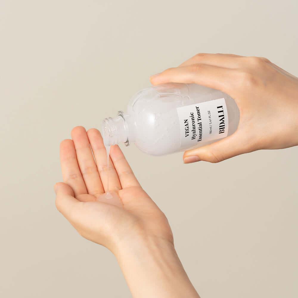 Hands pouring Bidalli Vegan Hyaluronic Essential Toner onto palm, lightweight vegan toner for deep hydration and daily moisturizing skincare routine, 160ml
